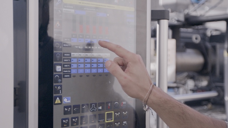 Close-up of someone's hand using the control panel of a biopolymer production machine